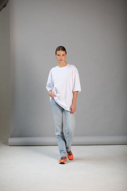 Une belle fille blonde dans un t shirt blanc surdimensionné et un jean bleu posant sur un fond