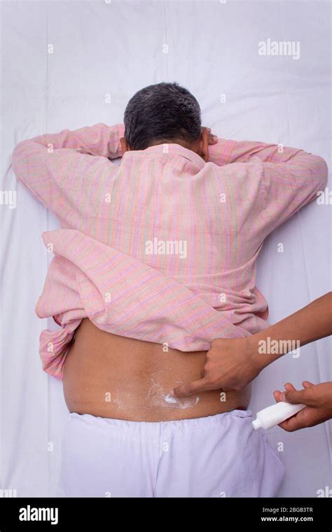 Man suffering from back pain, applying pain relief cream on man's back ...