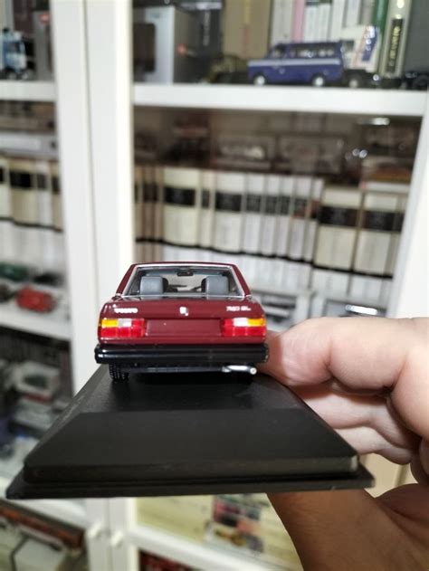 A Hand Holding A Toy Car On Top Of A Black Piece Of Paper In Front Of