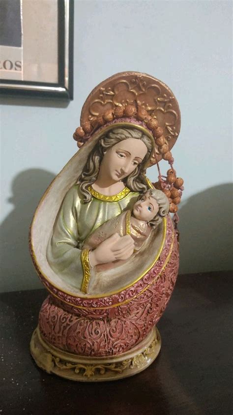 A Figurine Of The Virgin Mary Holding A Baby Jesus In Her Arms On A Table