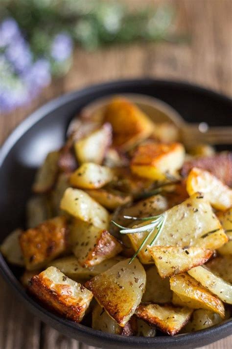 A Bowl Filled With Potatoes And Herbs On Top Of A Wooden Table