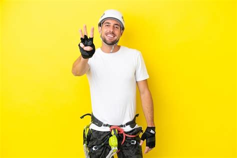 Homem jovem alpinista isolado em um fundo amarelo feliz e contando três