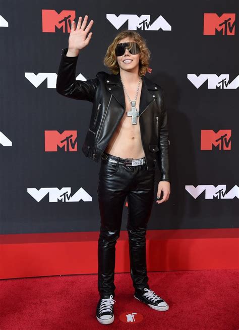 A Man In Black Leather Pants And Sunglasses Waves To The Crowd At An