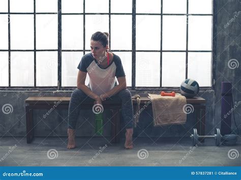 Woman Resting Elbows On Knees While Sitting On Bench In Loft Gym Stock