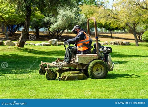 Man Mowing Or Cutting The Long Green Grass With A Green Lawn Mower In