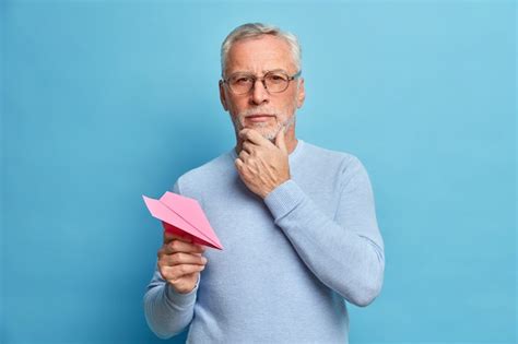 진지한 수염 난 남자 연금 수령자의 절반 길이 샷은 턱을 잡고 정면에서 직접 보이는 분홍색 수제 항공기를 캐주얼하게 옷을 입고