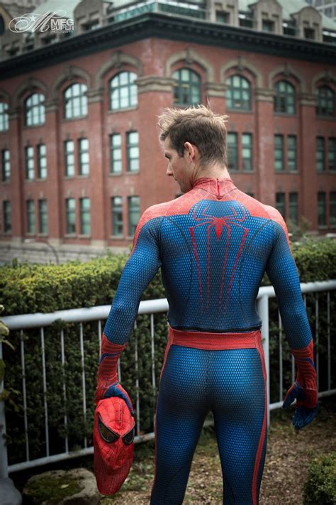 A Man In A Blue And Red Spider Suit Standing Next To A Fence With His