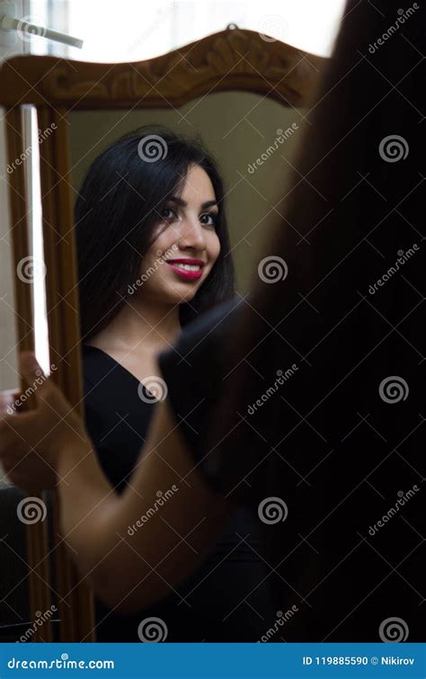 Young Charming Brunette Girl Looks At Her Reflection In The Mirror