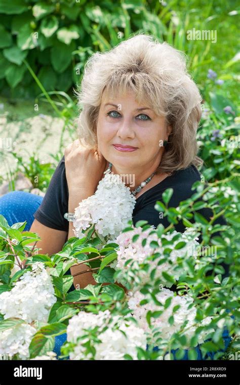 60 Year Old Woman In The Garden A Mature Woman Enjoys The Flowers Of A Hydrangea Grown With Her