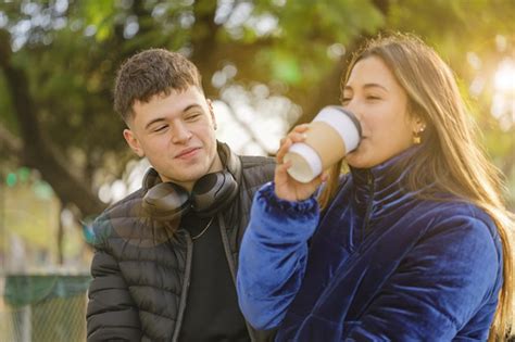 Chico mirando a una chica latina bebiendo café en el banco de un parque público Foto Premium
