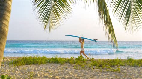 Young Woman On Fun Surfing Trip In Barbados Carries A Surfboard On Her