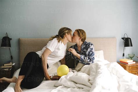 Lesbian Woman With Birthday Present Kissing Girlfriend On Bed At Home