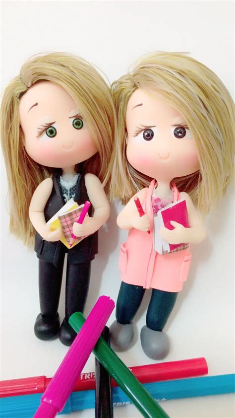 Two Dolls Standing Next To Each Other With Pens And Pencils In Front Of