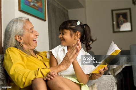 Grandmother And Granddaughter Having Fun Reading Book At Home Stock