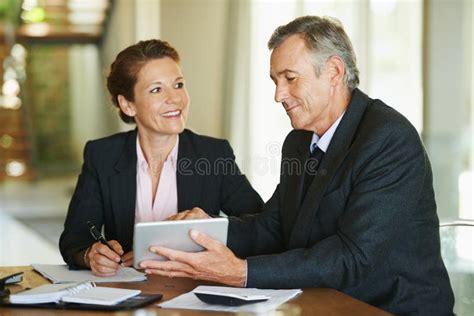 Look At These Figures Two Mature Businesspeople Using A Digital Tablet While Working Together