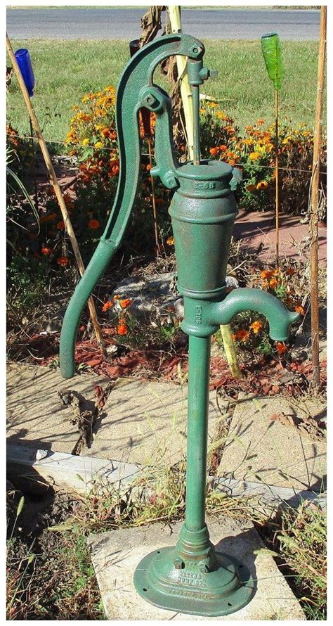 An Old Fashioned Green Water Pump In Front Of Some Flowers