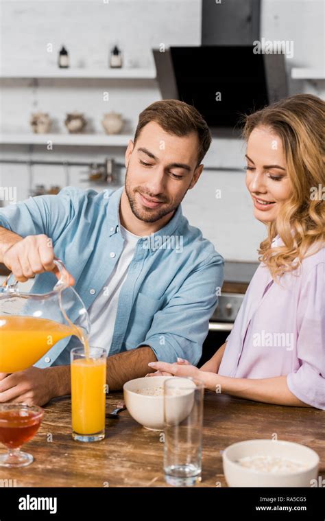 Smiling Man Pouring Orange Juice In Glass For Pretty Wife Stock Photo