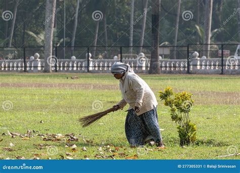 A Female Sanitation Worker Sweeping The Gardens Of An Old Monument With