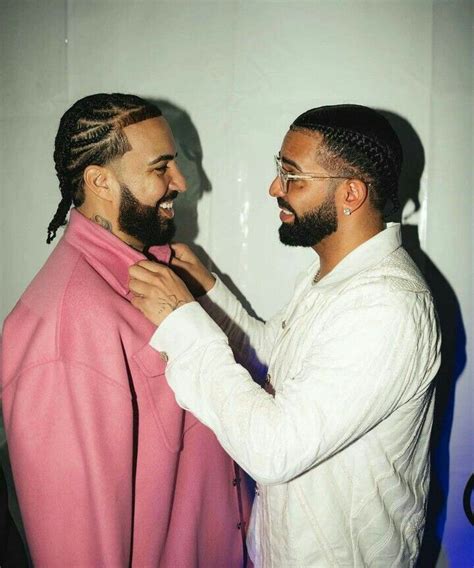 Two Men Standing Next To Each Other In Front Of A White Wall And One Is