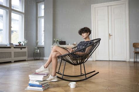 Young Woman Sitting On Rocking Chair At Home Reading A Book Stock Photo