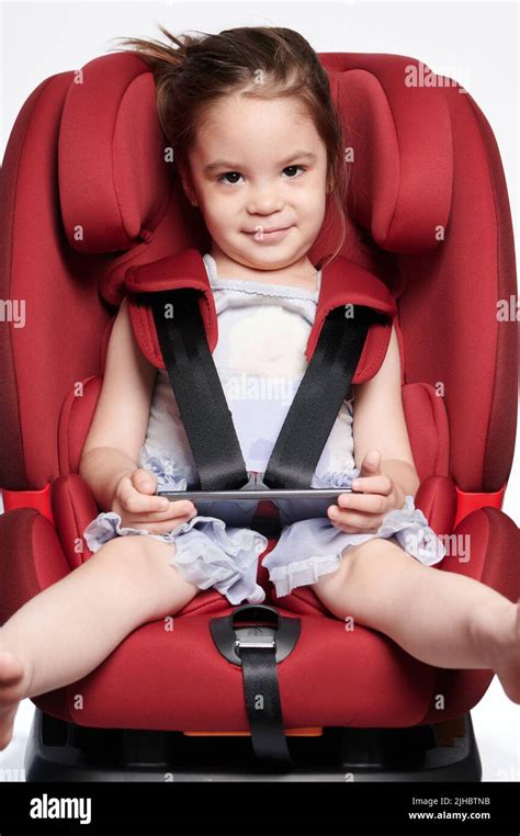 Girl In Car Seat Buckled With Smartphone Isolated On Studio Background