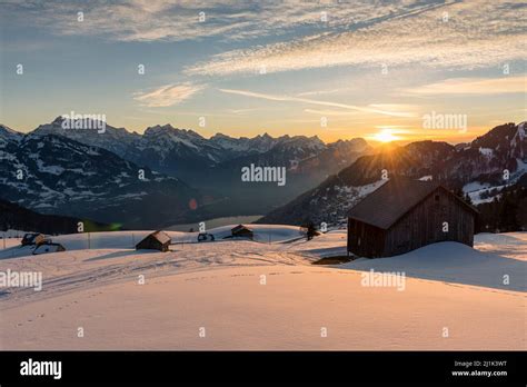 Snow Covered Mountain Meadows With Hay Huts In Front Of The Panorama Of