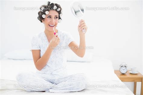 Cheerful Brunette In Hair Rollers Holding Hand Mirror And Applying Lip