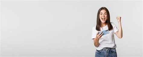Free Photo Attractive Cheerful Brunette Girl Winning In Mobile Game Holding Smartphone And