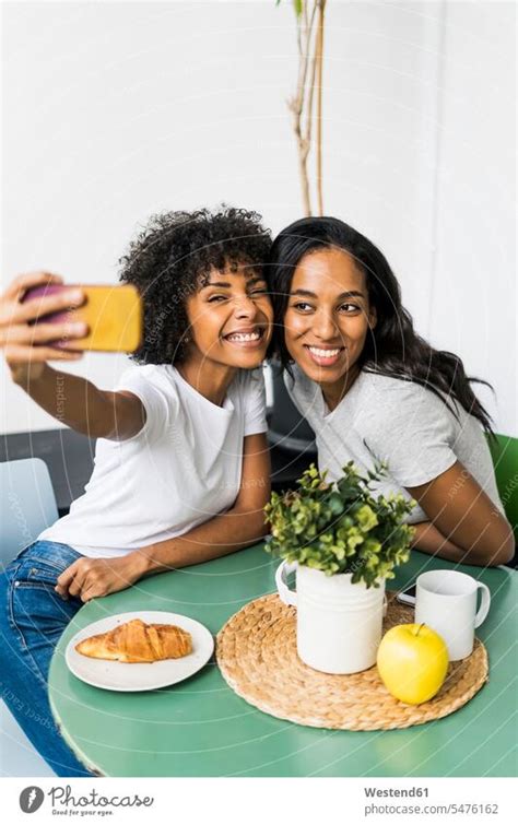 Zwei glückliche Freundinnen sitzen am Tisch und machen ein Selfie ein