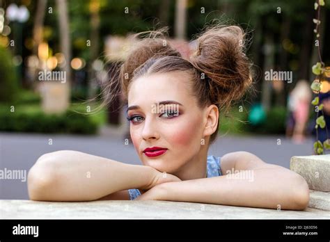 A Young Girl With Bright Pin Up Makeup Stands In The Park Leaning On A