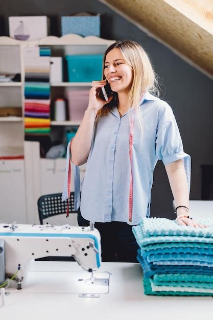 Mujer sonriente costurera hablando por teléfono móvil en su taller de