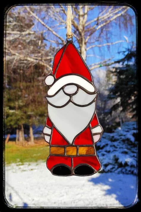 A Stained Glass Santa Clause Ornament Hanging From A Tree In Front Of