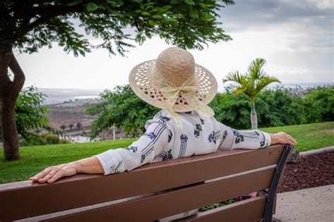 Vista Trasera De Una Anciana Relajada Con Sombrero Sentada En Un Banco