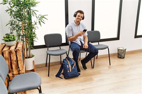 Young Hispanic Man Listening To Music Sitting On Chair At Waiting Room