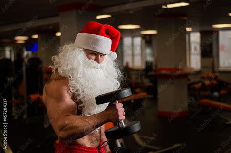 Santa Claus In The Gym Muscular Man With A Naked Torso Doing Exercises With Dumbbells Stock