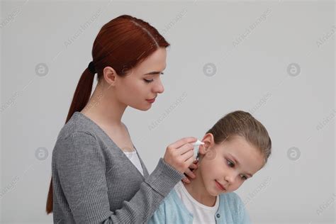 Mother Dripping Medication Into Daughters Ear On Light Grey Background