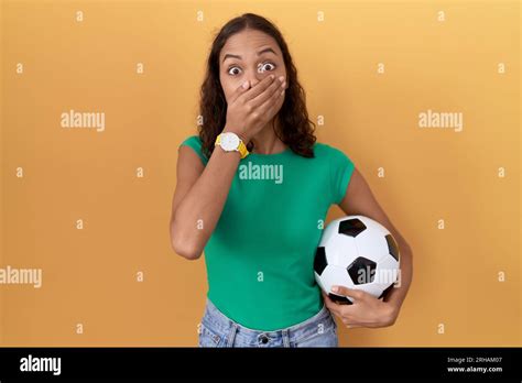 Young Hispanic Woman Holding Ball Shocked Covering Mouth With Hands For