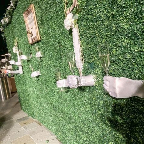 A Wall Covered In Fake Grass With White Gloves And Champagne Glasses On