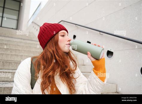 Smiling Traveler Redhead Girl Tourist Sits On Stairs With Flask Drinks Hot Coffee From Thermos