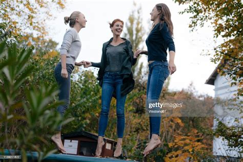 Happy Mother With Two Teenage Girls Jumping On Trampoline In Garden In