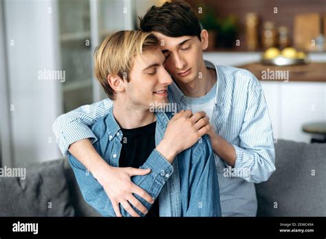 Homosexual Guys Loving Gay Couple Sitting At Home Tenderly Hugging