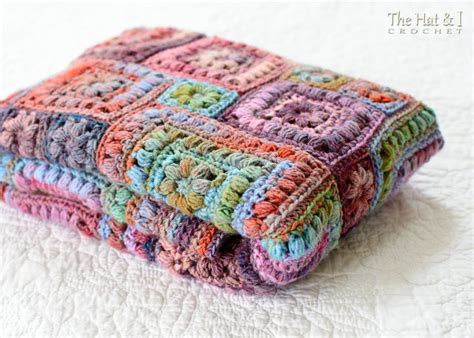 A Multicolored Crocheted Blanket Is Laying On A White Bed With It S