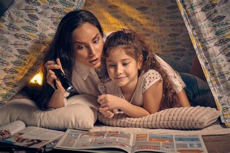 Mãe e filha estão sentadas em uma tenda lendo histórias a lanterna