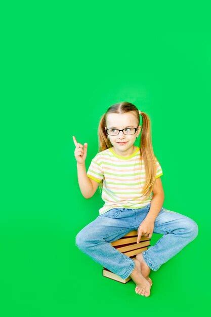 Uma menina senta se em um fundo verde em livros óculos e aponta o