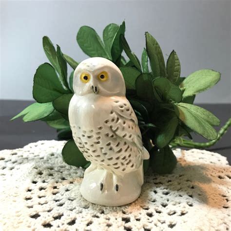 An Owl Figurine Sitting On Top Of A Doily Next To A Plant