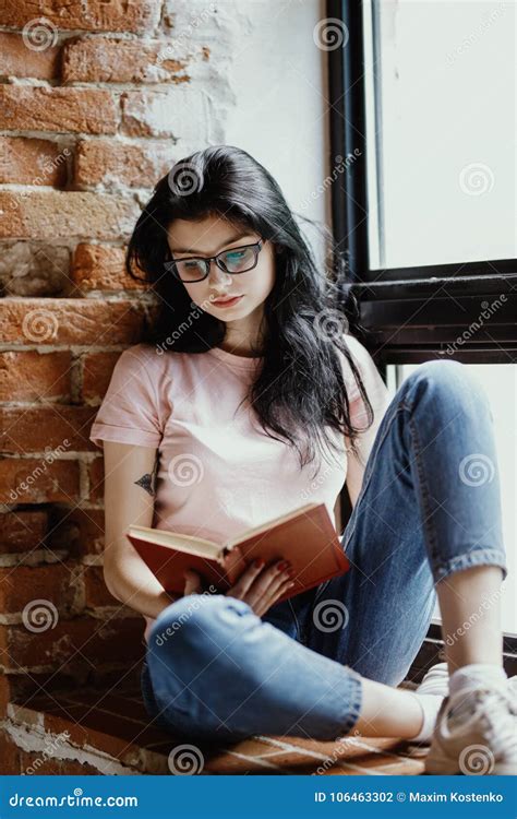 Beautiful Young Brunette Woman Reading Book Near Window At Home Stock