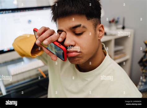 Brunette Teenage Boy Rubbing His Eyes While Using Cellphone In Bedroom Stock Photo Alamy