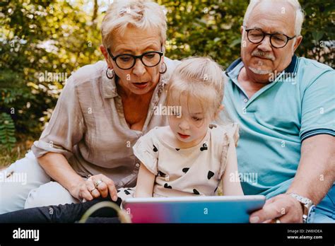 Granddaughter Reading Book While Sitting With Grandparents At Park