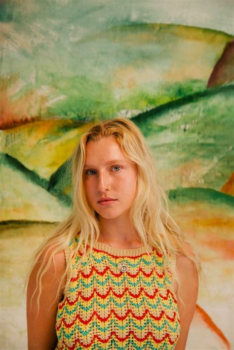 A Woman Standing In Front Of A Painting With Long Blonde Hair Wearing A