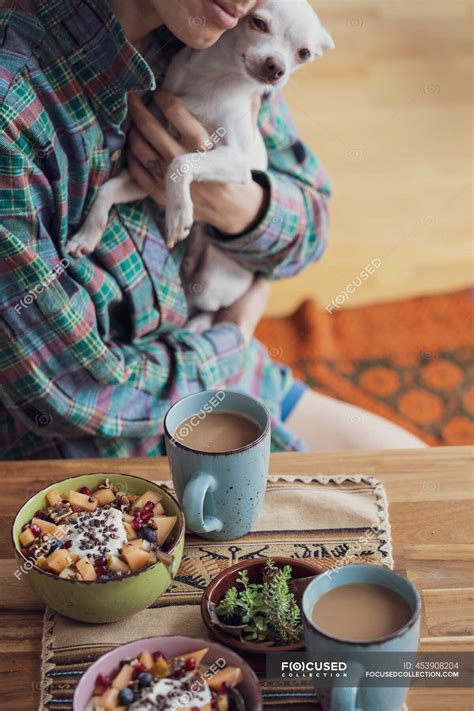 Person cuddles cute puppy dog at table with healthy breakfast & coffee